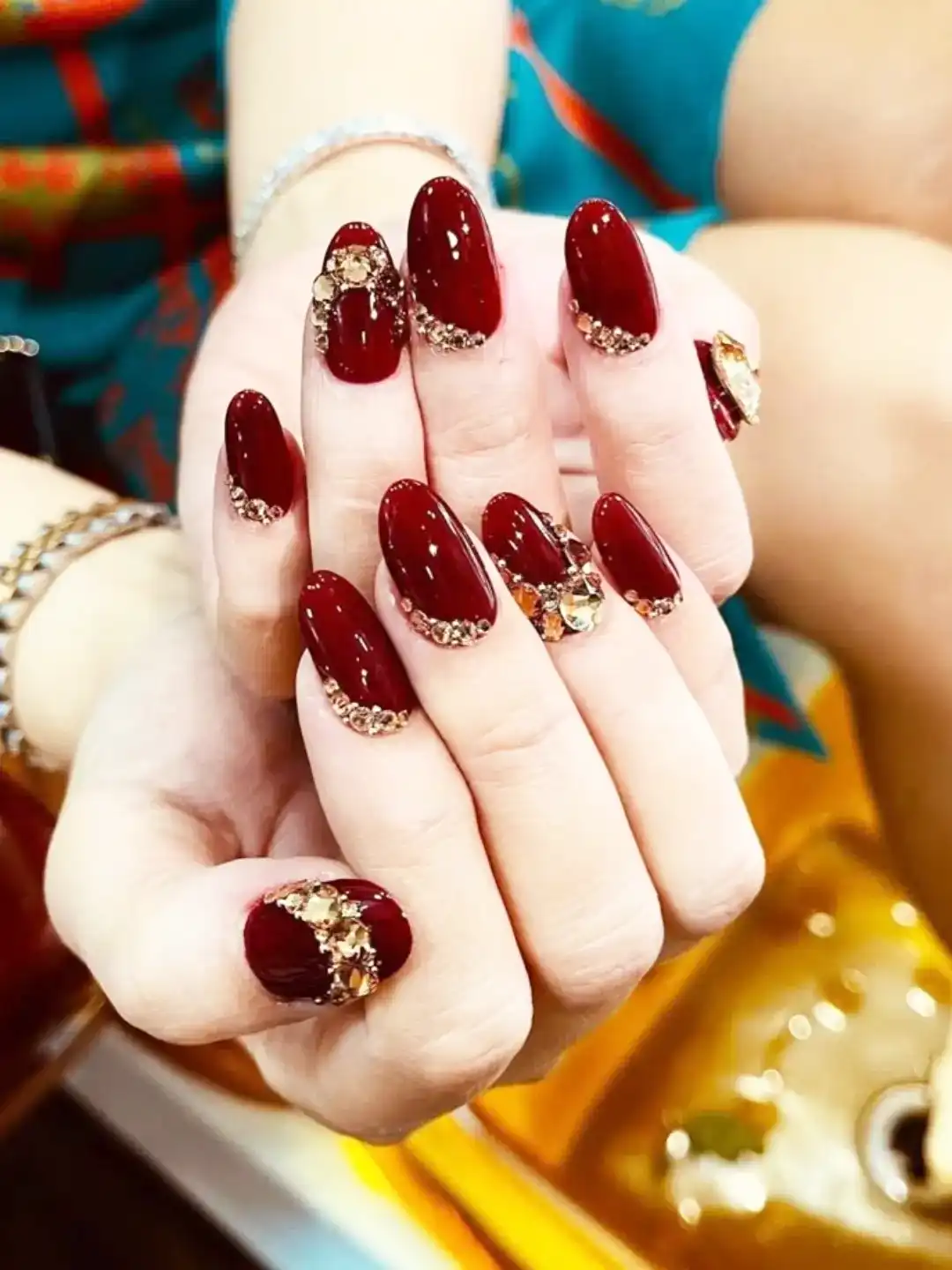 Glossy maroon nails with gold-toned rhinestone cuticle clusters