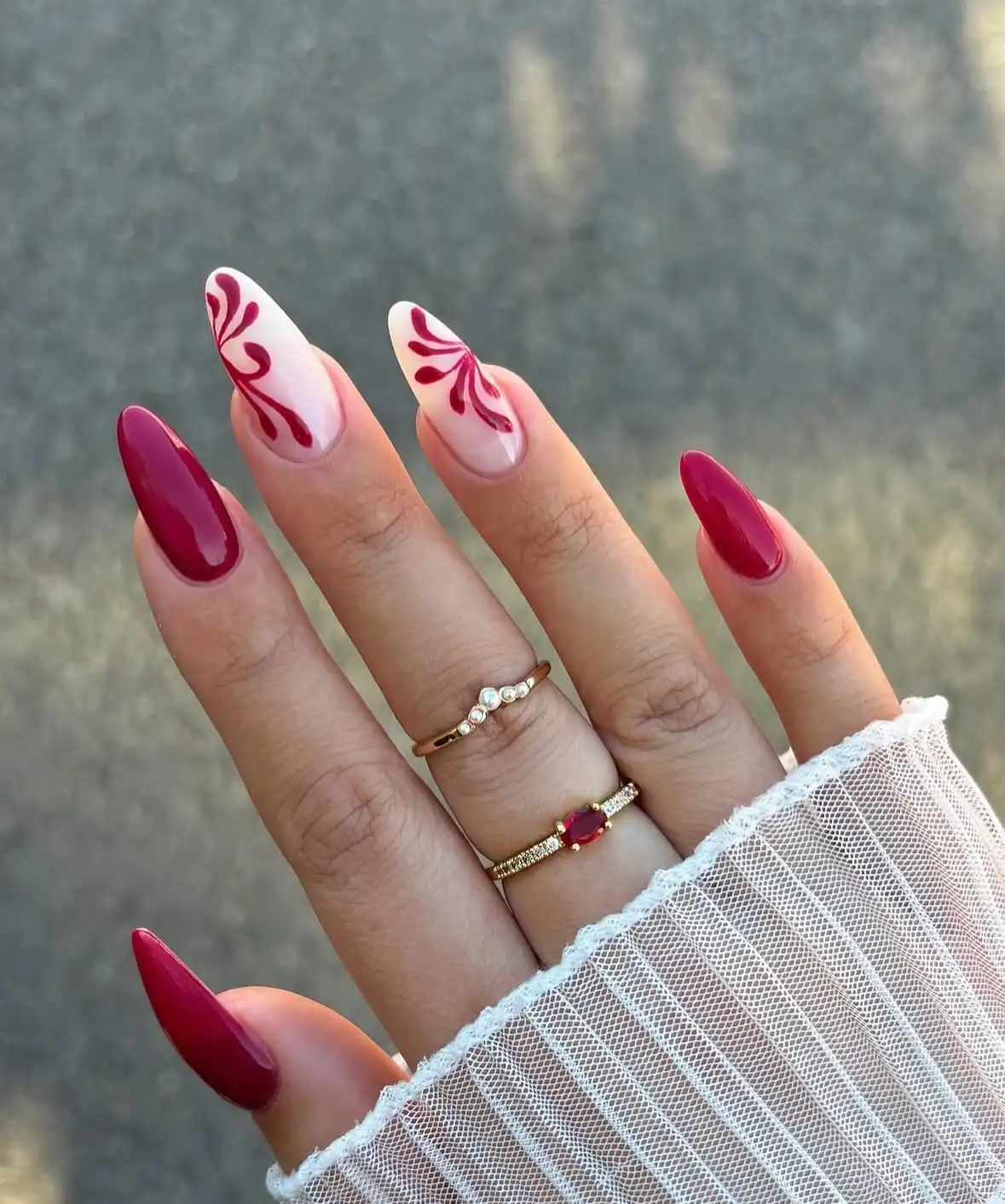 Glossy maroon almond nails with nude botanical swirl accents
