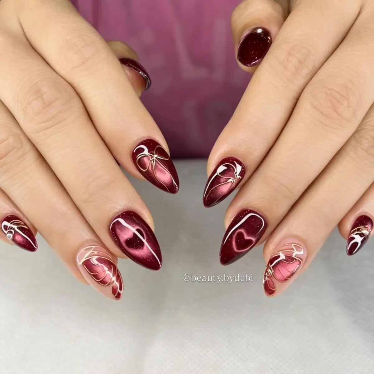 Metallic maroon stiletto nails with white abstract line art and heart detail