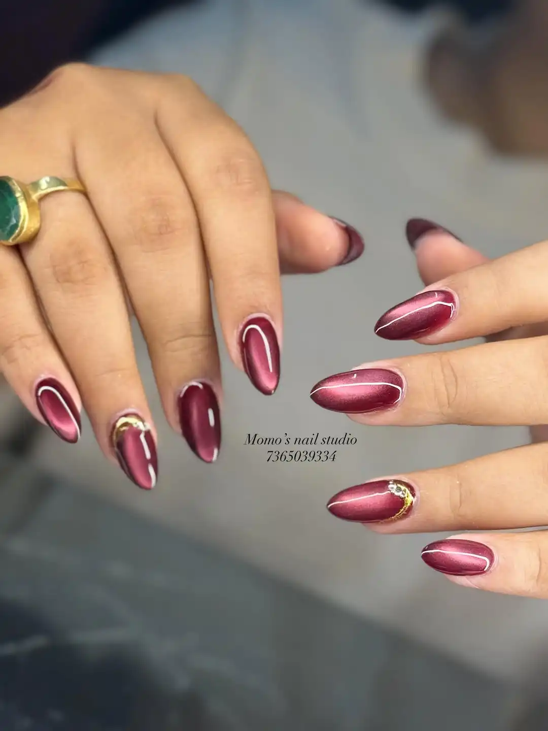 Metallic maroon pointed nails with central highlight stripe and gold crescent accents