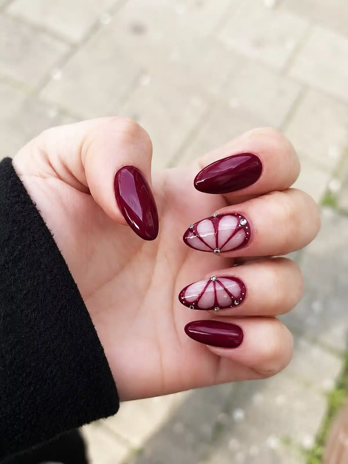 Glossy maroon almond nails with nude fan-line accents and silver studs