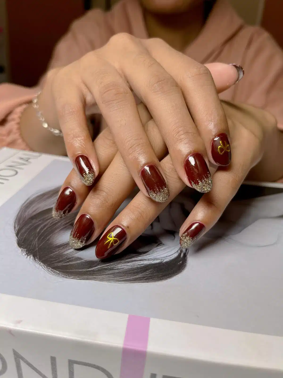 Glossy maroon nails with gold glitter tips and bow accents