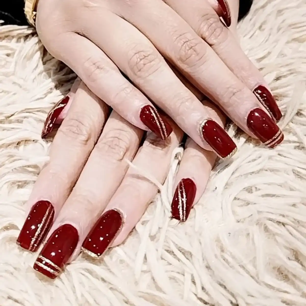 Square maroon nails with thin gold striping and subtle glitter