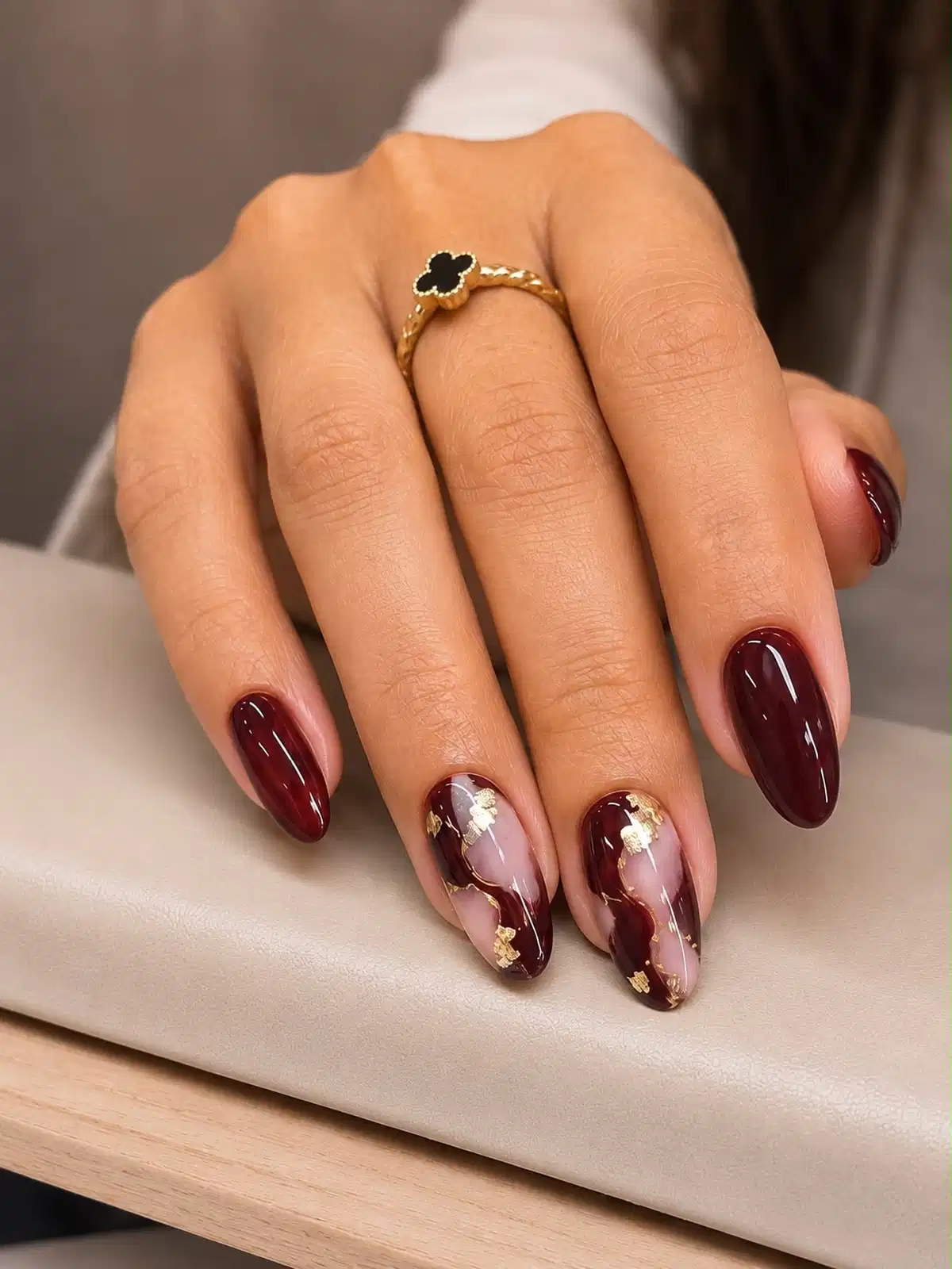 Maroon almond nails with nude swirl accents and gold foil patches