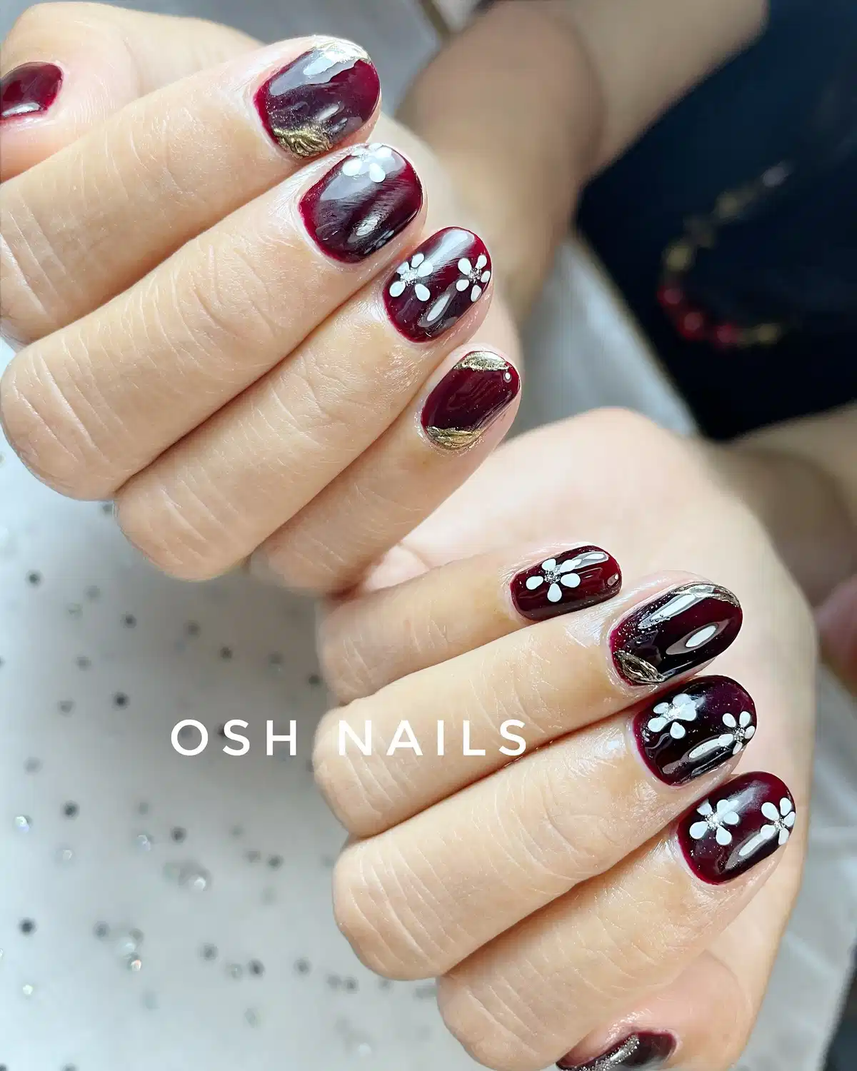 Maroon nails with white flowers and gold accents