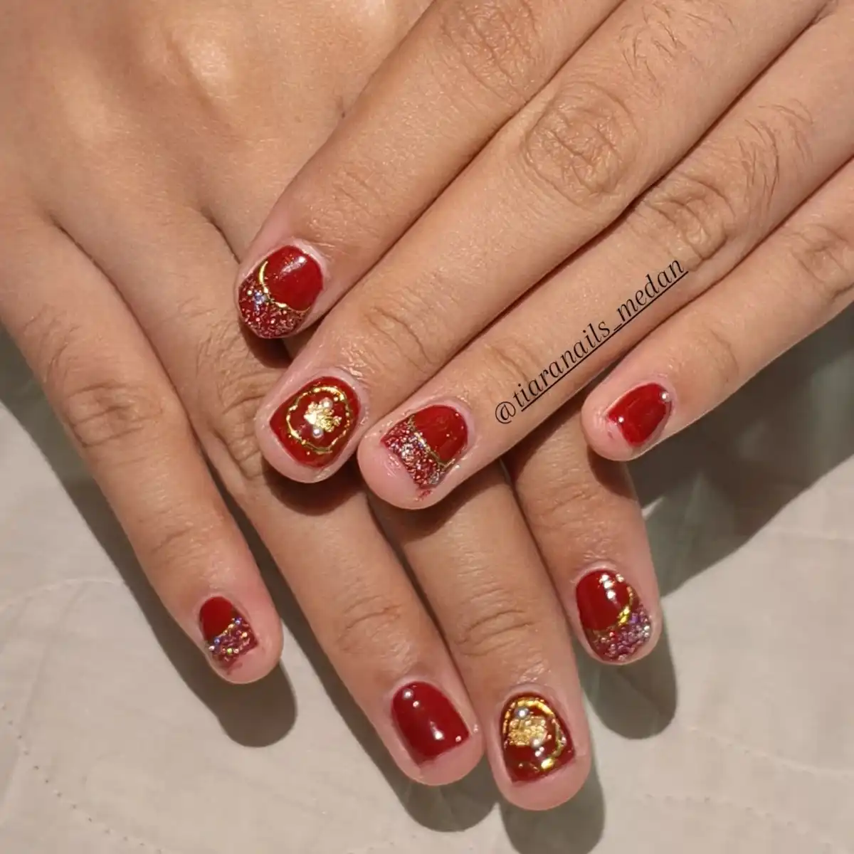 Short red-maroon nails with glitter bands and gold details