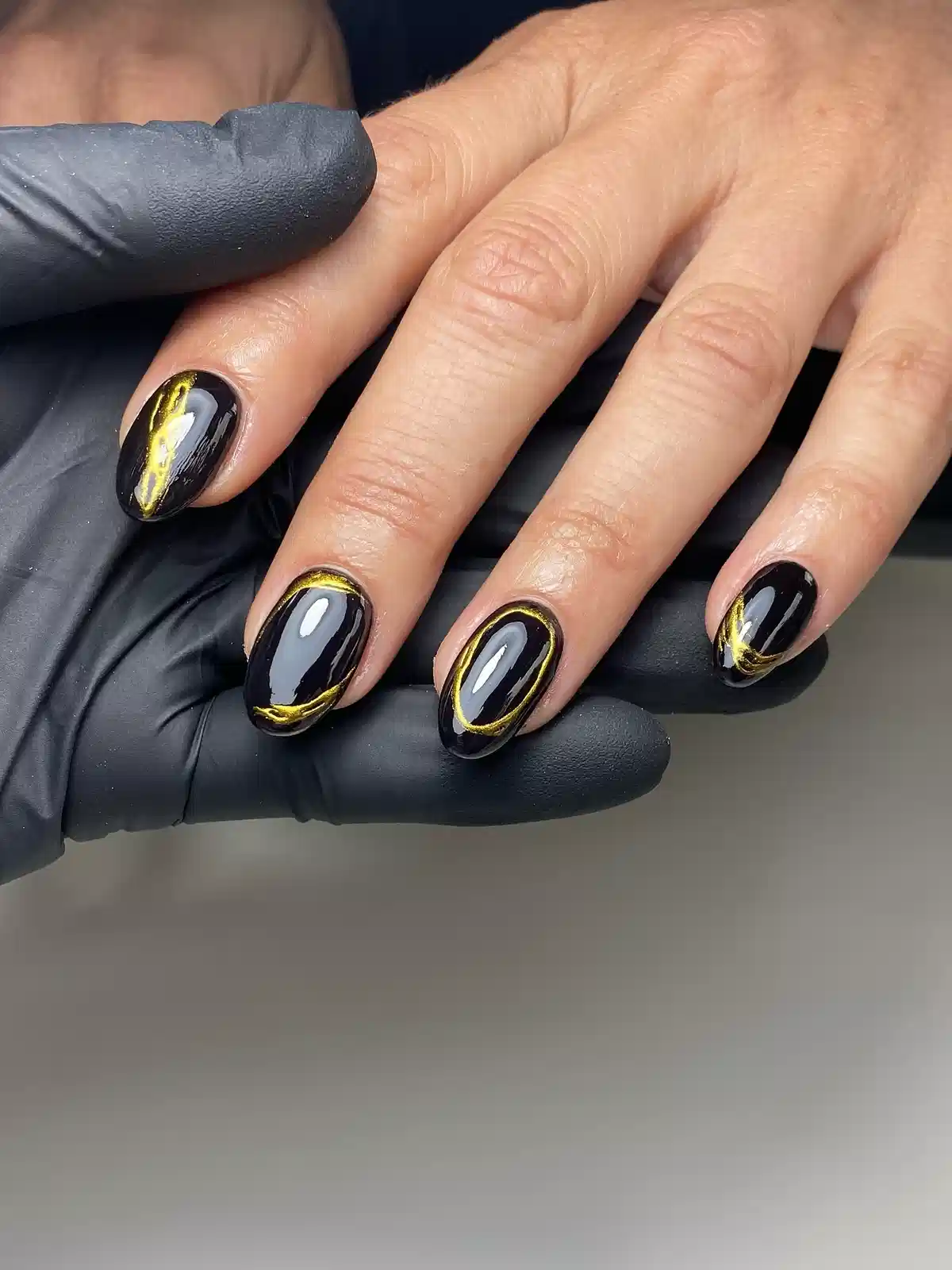 Glossy black nails with thin gold outlines and a gold streak accent