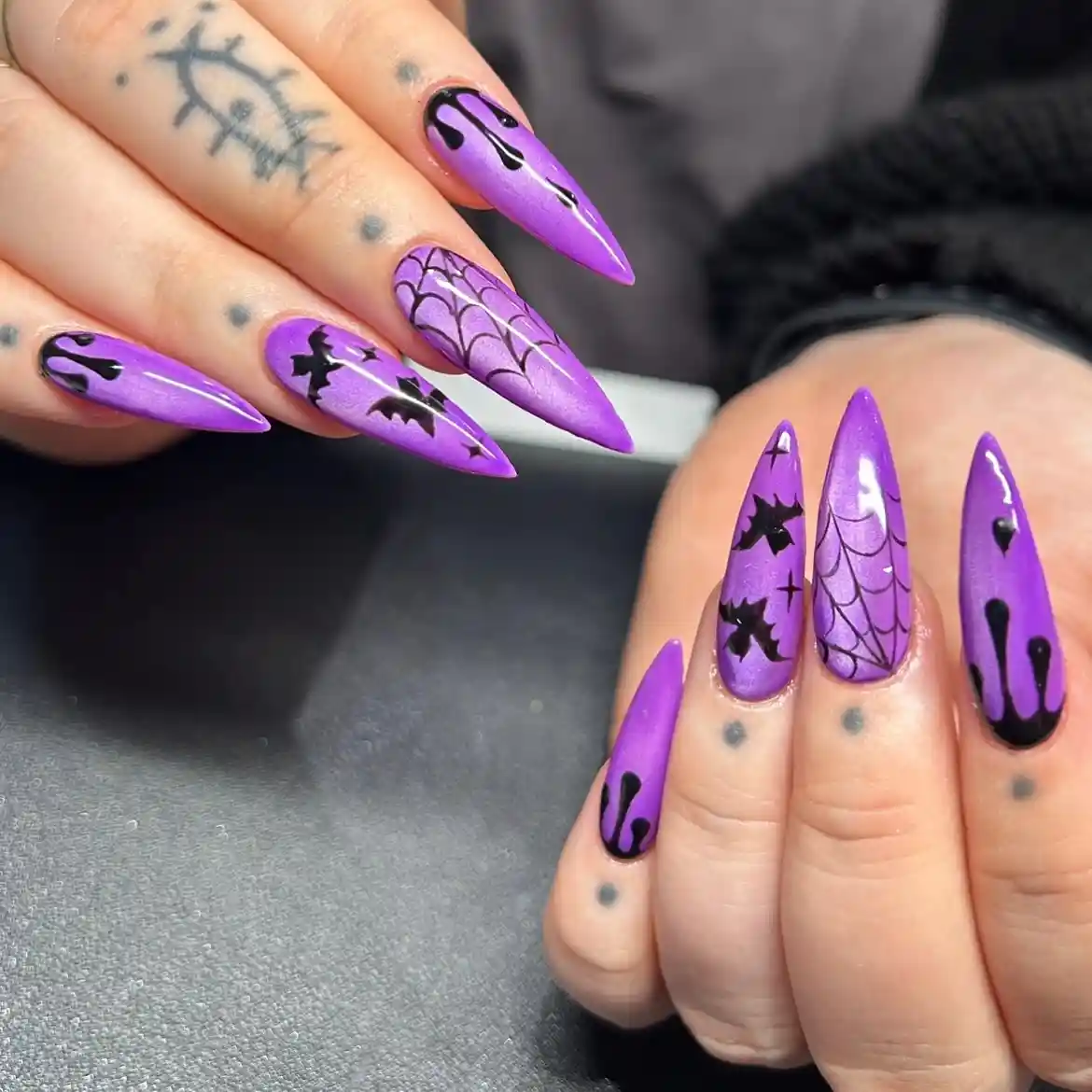 Purple stiletto nails with black drips, bats, and web lines