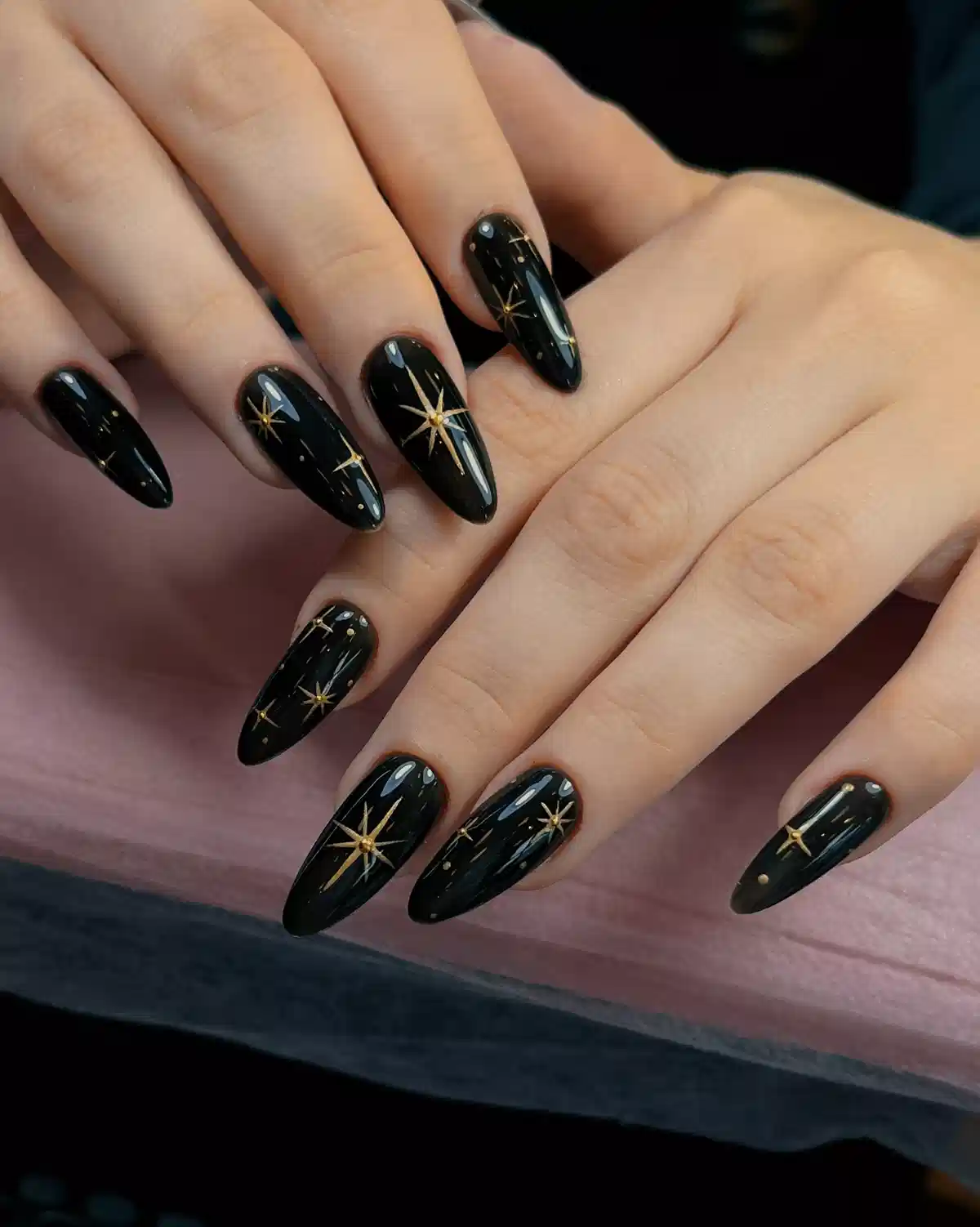 Glossy black almond nails with gold starburst and dot accents