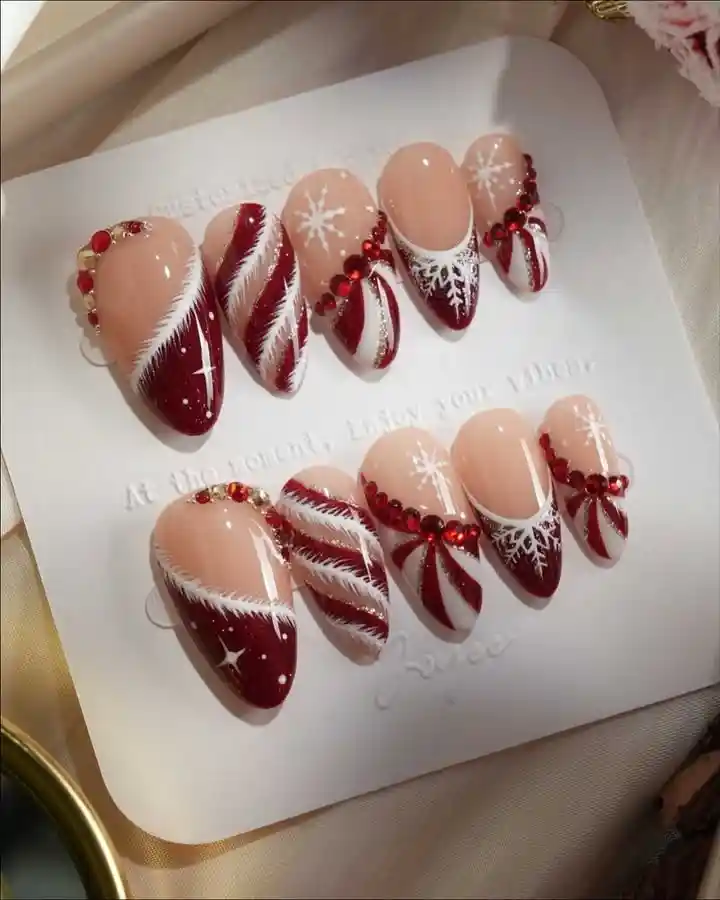 Nude-and-deep-red almond tips with snowflakes and rhinestone clusters