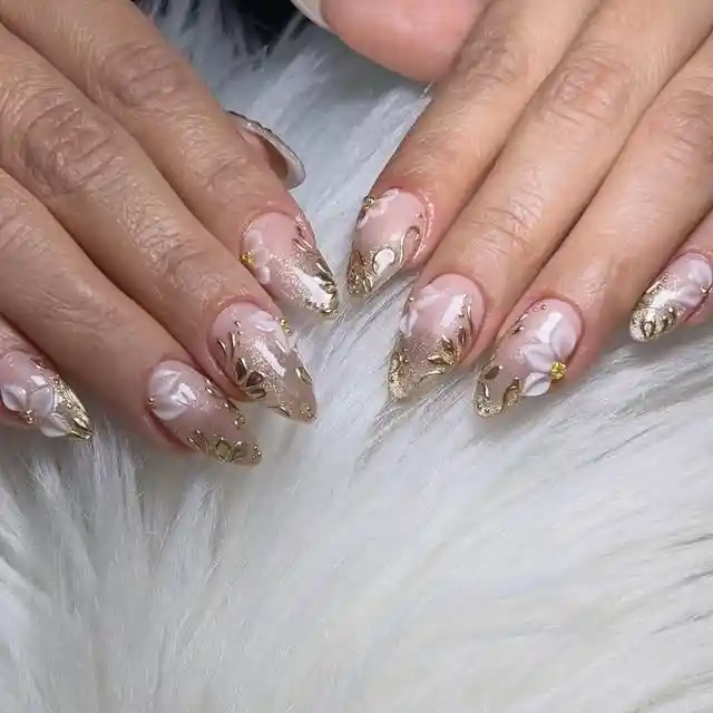 Nude almond nails with gold foil-like accents and white florals