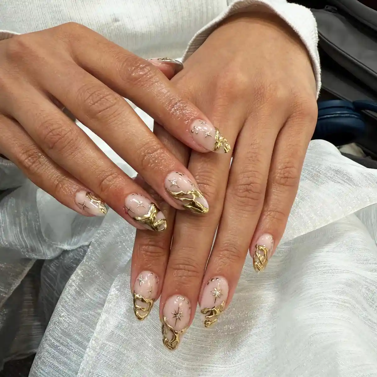Almond nude nails with raised gold accents and starbursts