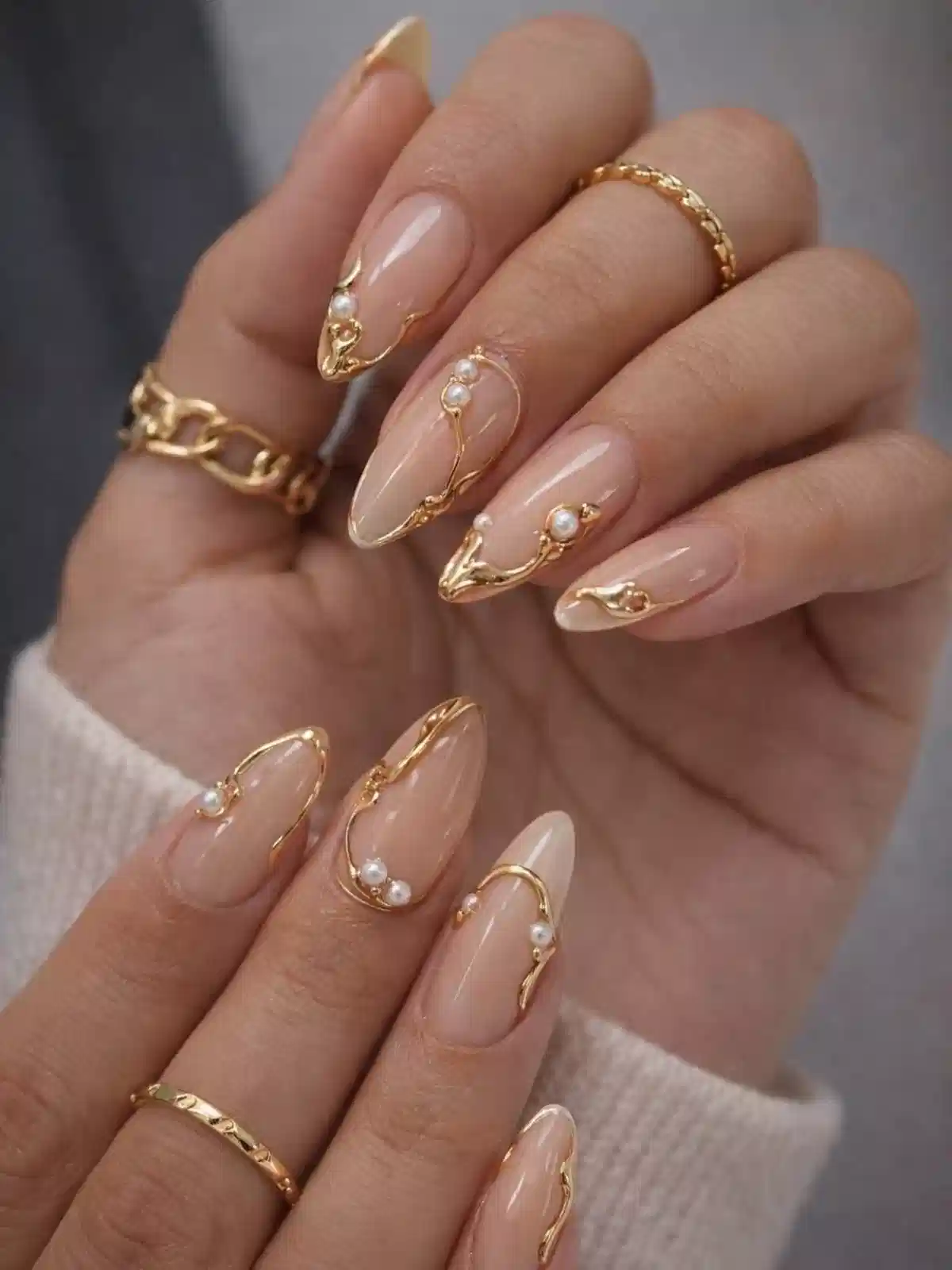 Glossy nude almond nails with raised gold outlines and pearls