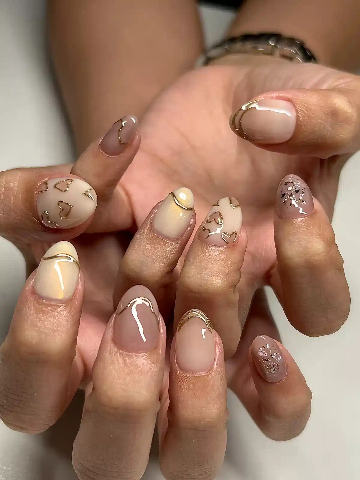 Glossy nude nails with gold heart outlines and glitter accents