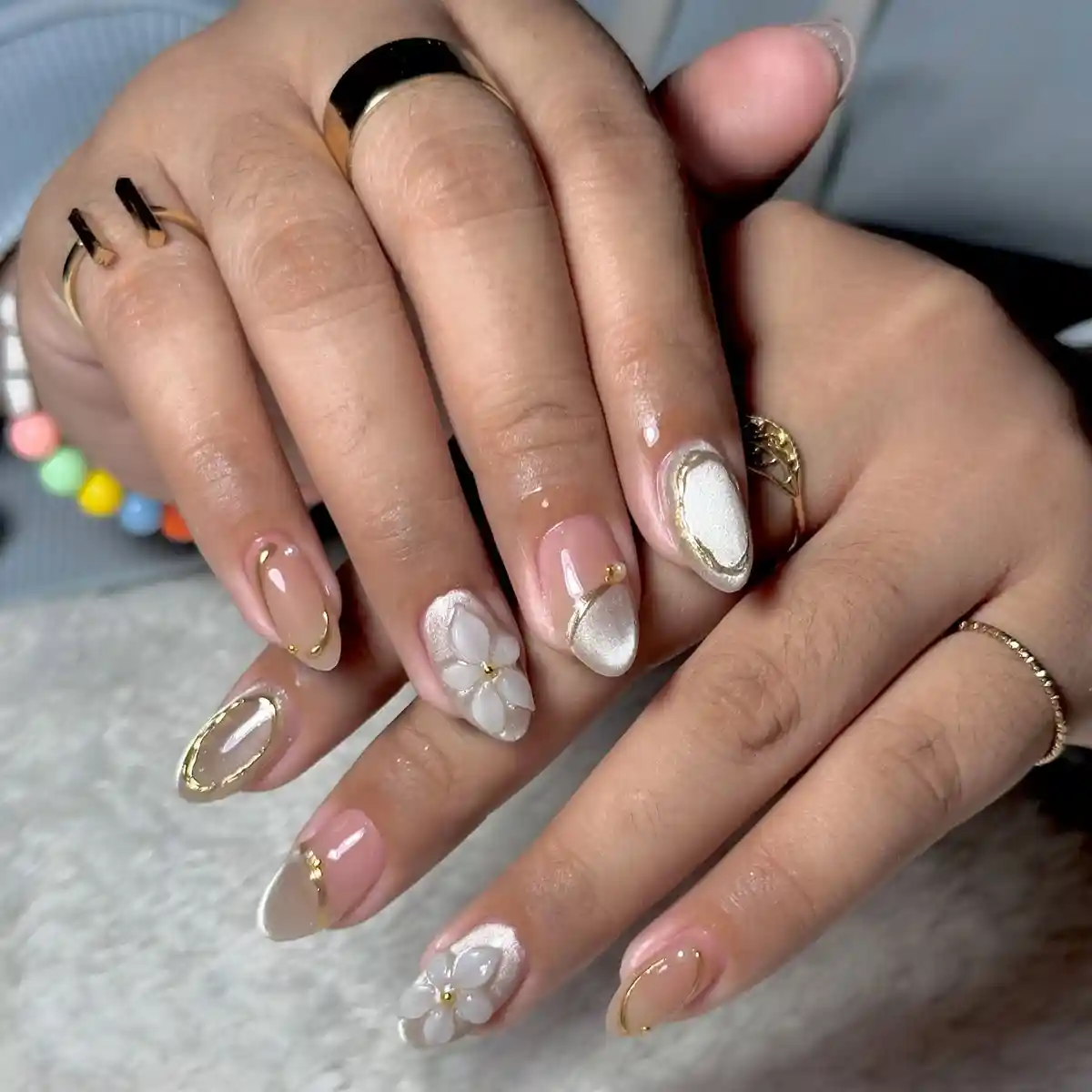 Nude almond nails with gold outlines and 3D white flowers