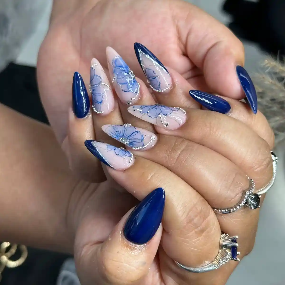 Navy stiletto nails with blue floral line art and rhinestone accents