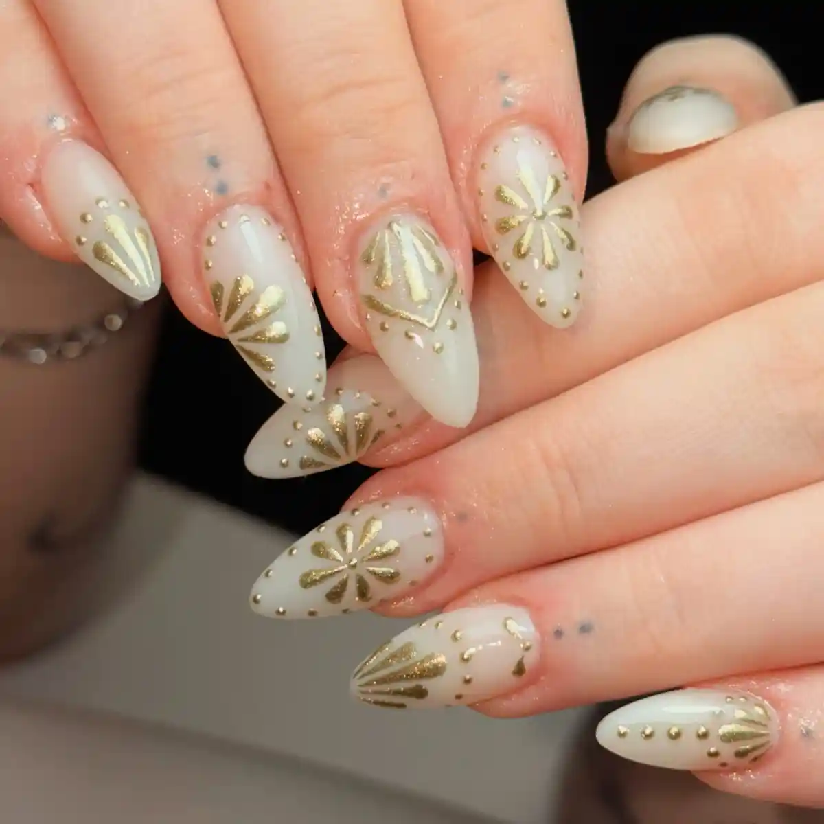 Milky white pointed nails with gold motifs and stud detailing