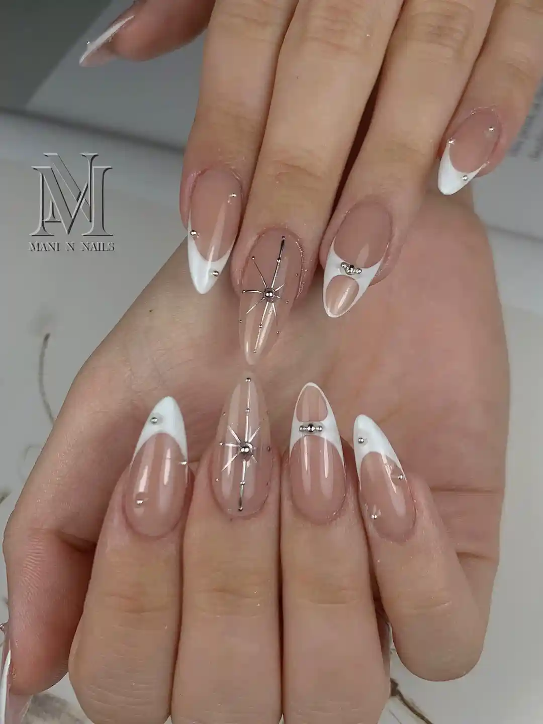 Nude and white curved French tips with silver starburst accents