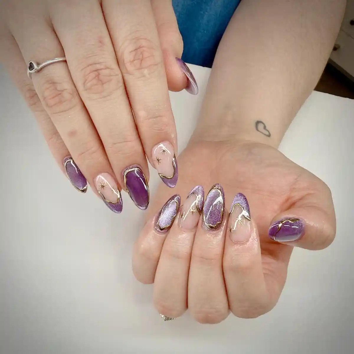 Purple shimmer and nude nails with gold outlines and starburst details