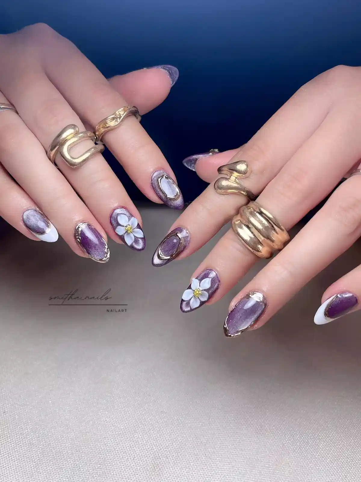 Purple metallic almond nails with white flowers and gold outlines