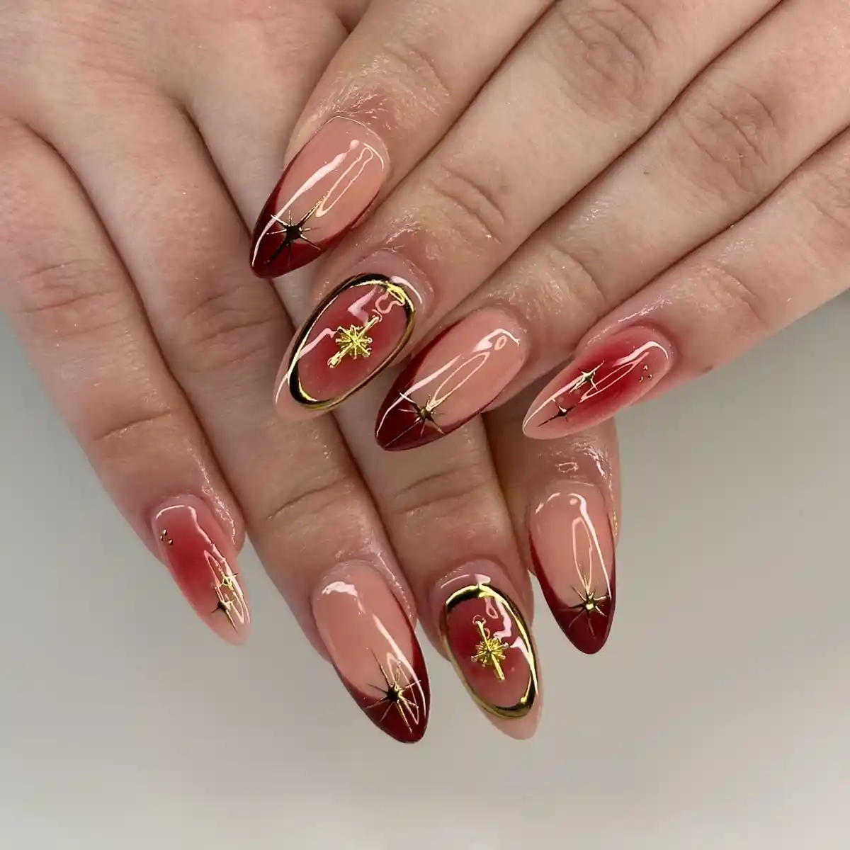 Nude-to-red gradient nails with starburst lines and framed charm accents