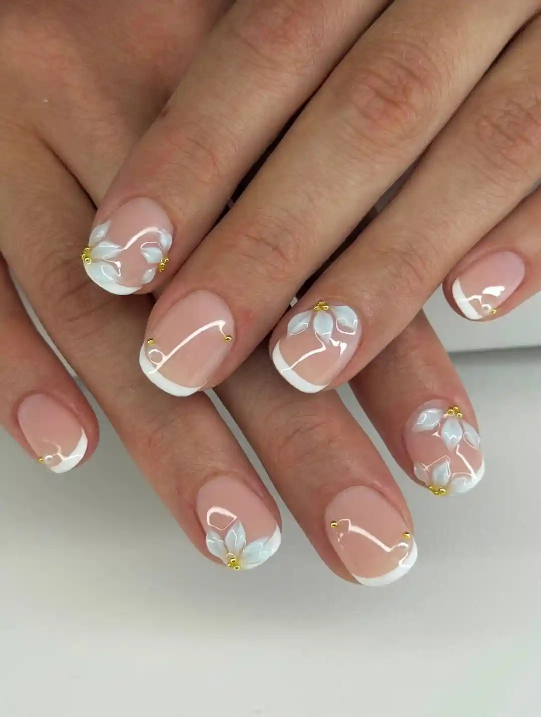Nude French tips with raised white floral details and gold beads